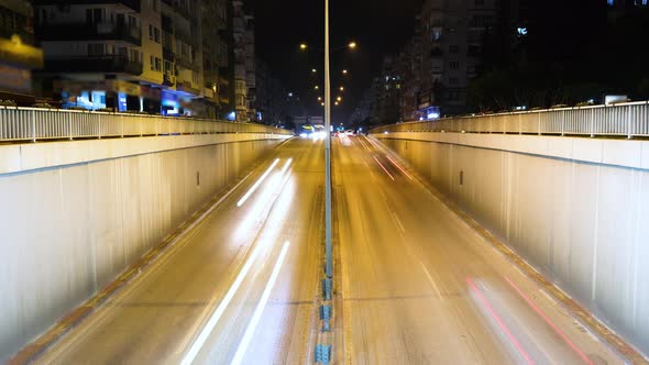 Night time-lapse, top view of a busy urban two-way road at the entrance to an underground tunnel.
