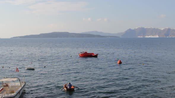 A man is paddling in the aegean sea, inside the Santorini caldera.