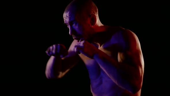 a Muscular Man with a Naked Torso is Boxing on a Dark Background
