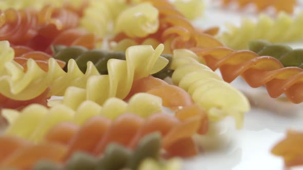 Colored uncooked pasta in a spiral shape close-up on a white plate