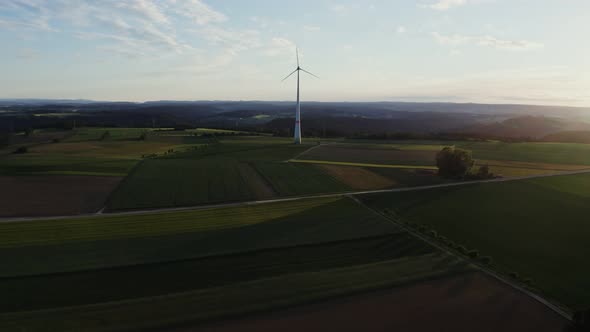 The Light of the Rising Sun Illuminates the Meadow on Which is Wind Generator