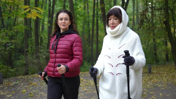 Two Mature Caucasian Women Talking Walking with Poles in Autumn Park Working Out