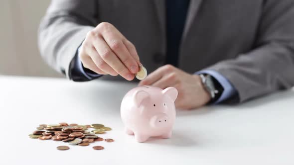 Close Up Of Man Putting Coins Into Piggy Bank 1