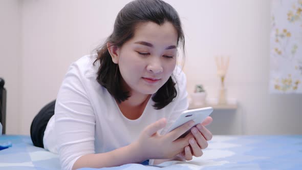 Asian woman looking and touching smartphone relax enjoy and smile with online social media in bedroo