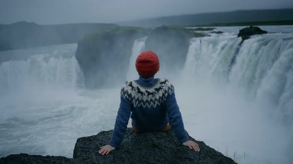 Man in Wool Sweater on Edge of Waterfall Rock