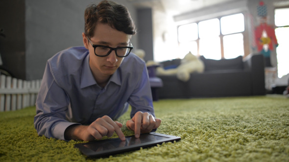 Man Typing on Tablet, Laying on Floor alt