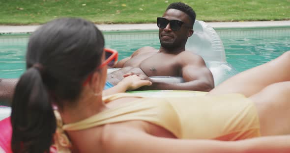 Happy diverse couple wearing swimming suits with inflatables at swimming pool in garden