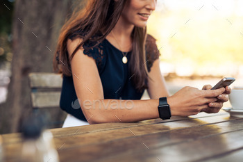 . Cropped image of young woman sitting at a table with a coffee using mobile phone.