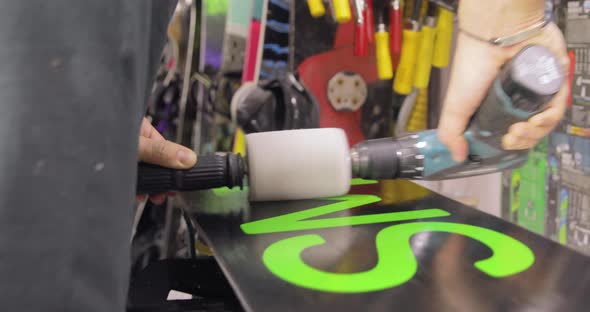 Repairman Is Polishing A Waxed Snowboard. Motion Toward And Backward