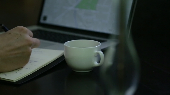Man Taking Notes From a Laptop With a Map On It
