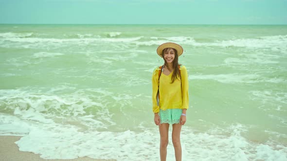 Camera Zooming Out of Happy Young Woman in Hat Standing on Waving Sea Background