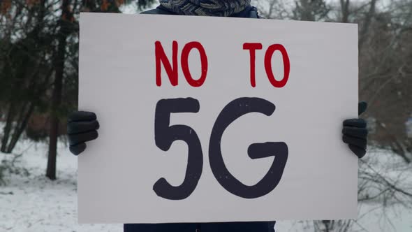 A person is standing in the park and protesting with a banner No To 5G. Picket