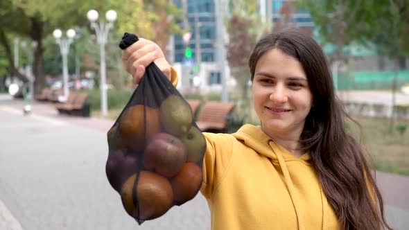 A Brunette Woman Shows a Fruit Mesh Fabric Bag with Vegetables and Fruits