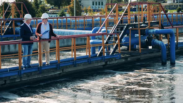 Two Engineers Are Talking Near Pipes of a Sewage Cleaning Site