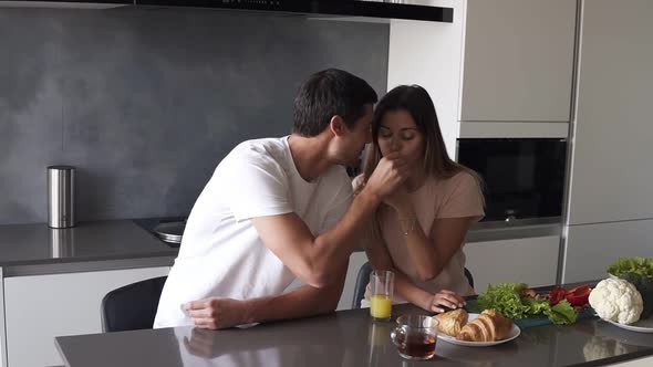 Young Man and Woman Eating Croissants Driking Tea and Talking Sitting at Table Counter in Kitchen