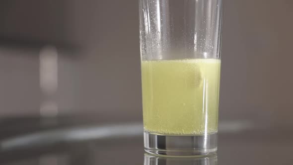 Vitamin C tablet is dissolving into a transparent glass of water. Slow motion