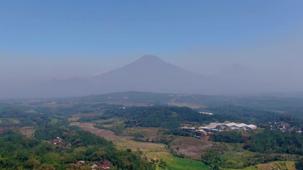 Silhouette of twin mountain peeks in far distance behind misty area, aerial drone view