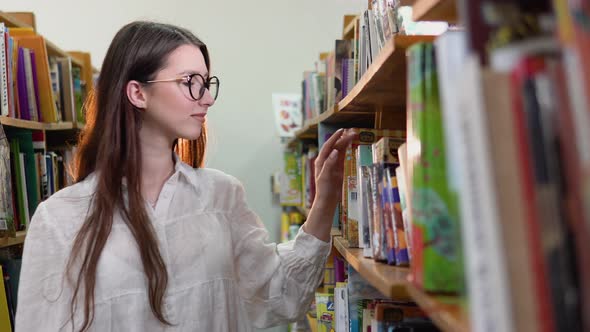 A University Student is Looking for a Book on Bookshelves in the Library