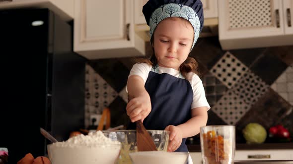 A Little Girl of Three Years in a Cap and Apron Prepares Dough for Cookies