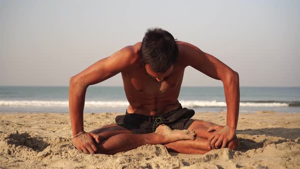 A Young Man Practices Yoga Outdoors Against the Background of the Sea