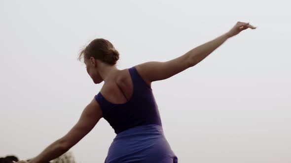 Female ballerina rehearses dance background sky, back view. Dancer trains outdoors. Woman dances