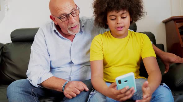 Grandson and grandfather sitting on couch using smartphone