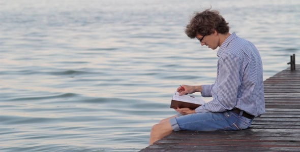 Man Writes In A Notebook Sitting By The River