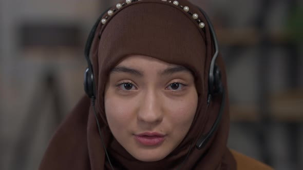 Headshot Portrait of Young Confident Middle Eastern Woman in Headphones and Hijab Talking Looking at