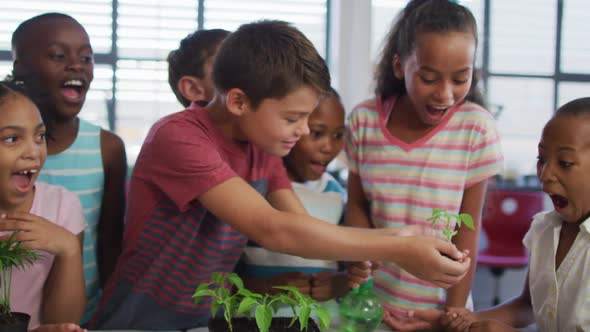 Diverse group of happy schoolchildren looking after plants in classroom during nature studies lesson