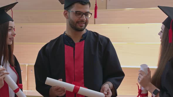 Three Graduates in Robes Holding Certificates, Talking.