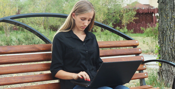 Young Girl Resting in a Park and Using Laptop alt