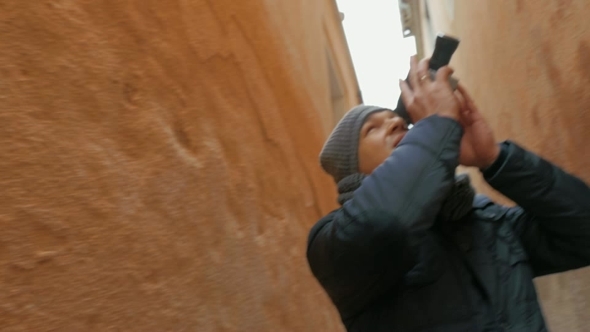 Man Walking Between Aged Houses With Retro Camera alt