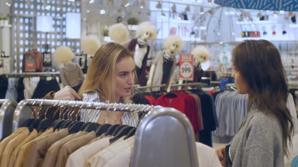 Pretty Brunette Choosing and Trying on a Jacket with Friend in Mall