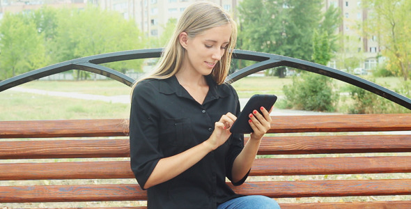 Girl Sits on a Bench in a Park and Using a Tablet alt