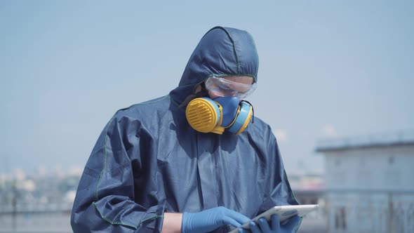 Portrait of Serious Man in Chemical Suit Using Tablet Outdoors. Young Confident Caucasian Specialist