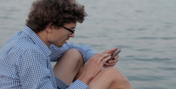 Man Uses The Phone On The Background Of The River alt