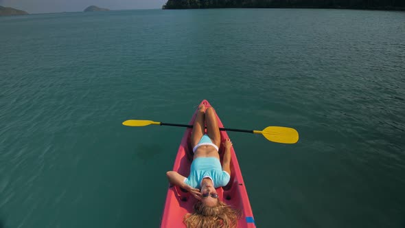 Pretty Slim Woman in Elegant Swimsuit Lies in Pink Plastic Kayak Drifting on Azure Ocean at Exotic