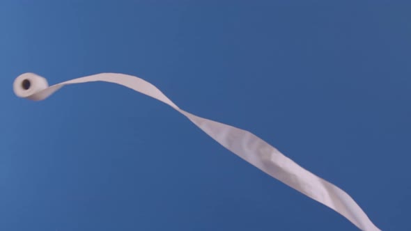 A toilet paper roll is seen flying through the air slowly in front of a blue backdrop.