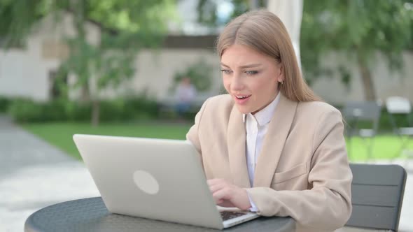 Young Businesswoman Celebrating Success on Laptop in Outdoor Cafe