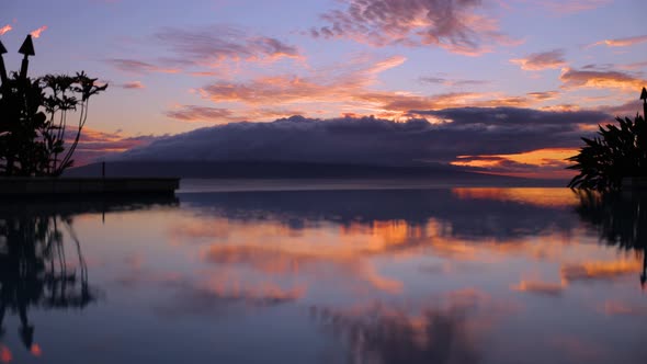 hawaiian infinity pool reflection of sunset behind lanai island with torches