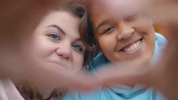 Close Up of Two Diverse Lesbians Making Heart with Hands Outdoors