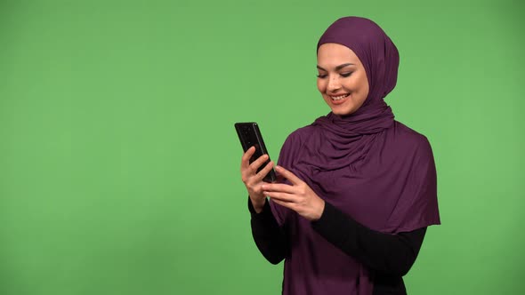 A Young Beautiful Muslim Woman Talks on a Video Call on a Smartphone with a Smile  Green Screen