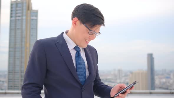 Business man use mobile phone on rooftop of high building with day light then express happy