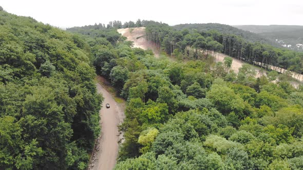 Aerial Top View Car Is Driving on a Bad Road in the Woods Between the Trees, Bypassing Potholes on