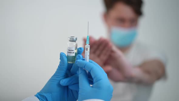 Coronavirus Vaccine Ampoule and Syringe with Blurred Man in Face Mask Refusing Vaccination