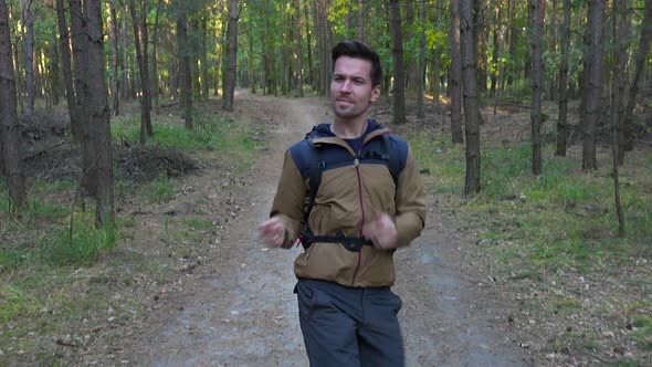 A Young Handsome Hiker Dances His Way Down a Path Through a Forest - Front View