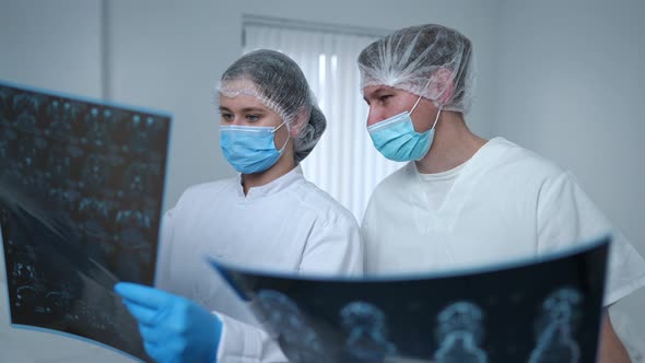 Troubled Serious Man and Woman in Medical Uniform Talking Analyzing Xrays Planning Treatment Surgery