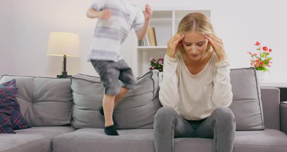 Tired Mom and Fun Son School Child Jumping on the Bed Exhaustion of the Mother From the Children Mom