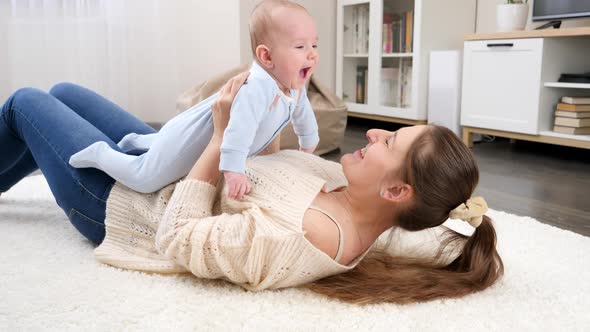Happy Smiling Mother with Little Baby Son Lying on Floor at Living Room and Having Fun