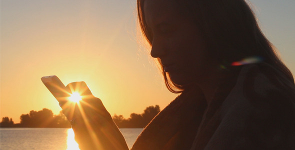 Girl on the Beach at Sunrise Using a Tablet